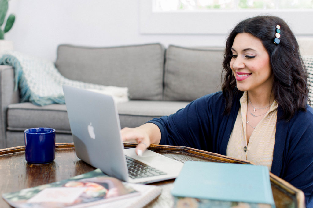 Dark-haired woman smiling at a laptop.