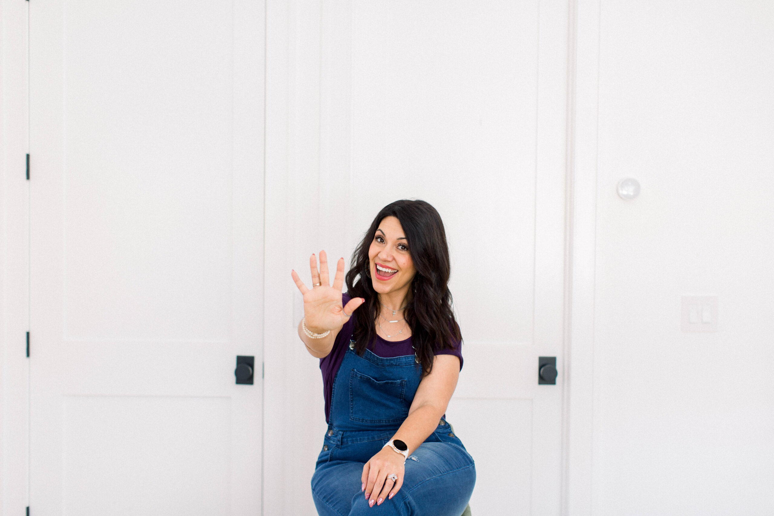 dark haired woman sitting against a white wall wearing a blue shirt and jeans. She is holding up her right hand with five fingers spread out. Title is 5 Steps to Creating a Passive Income Business Fueled by Your Podcast