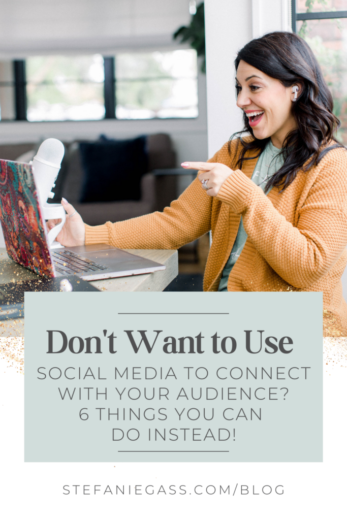 A long, dark-haired woman is pointing at her open laptop screen. There is a podcast microphone to the side of the laptop. She is wearing a tee with a mustard-colored cardigan. She has headphones in her ears. The title of the graphic is Don't Want to Use Social Media to Connect With Your Audience? 6 Things You Can Do Instead! The link at the bottom of the graphic is stefaniegass.com/blog