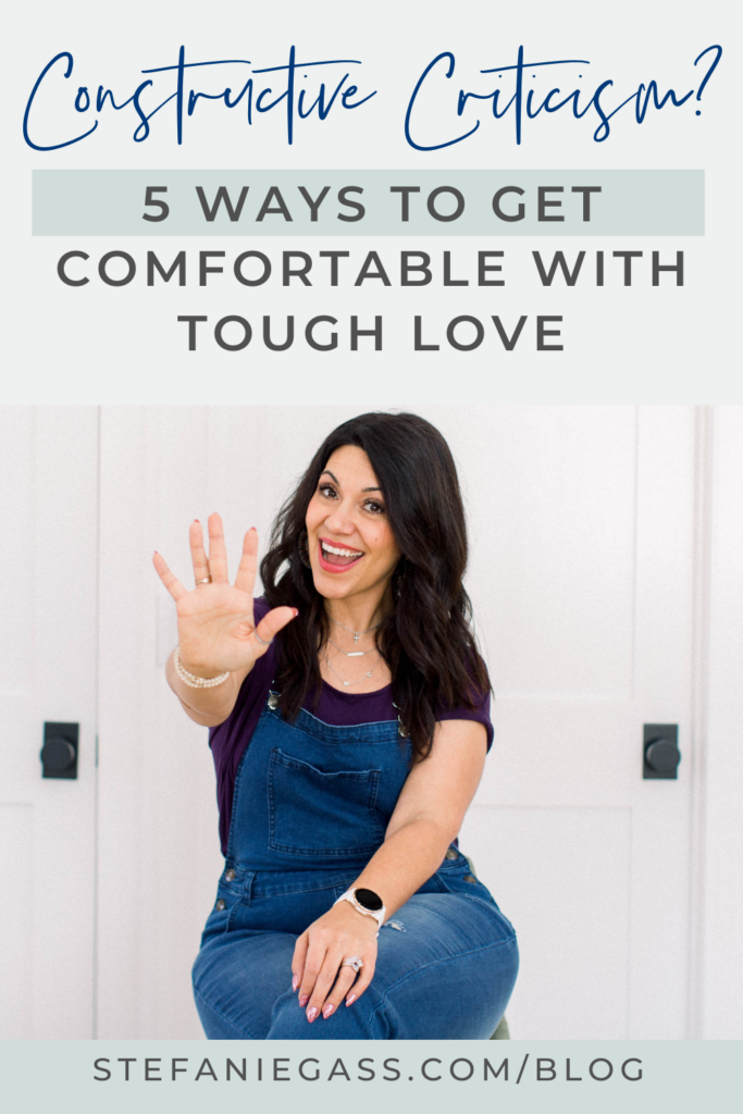 dark haired woman sitting on a stool in front of a door. She is wearing a purple shirt and denim overalls. Her left hand is on her knee and her right arm is raised in front of her with her five fingers display. The title at the top is, "Constructive Criticism? 5 Ways to Get Comfortable with Tough Love." The link at the bottom is stefaniegass.com/blog