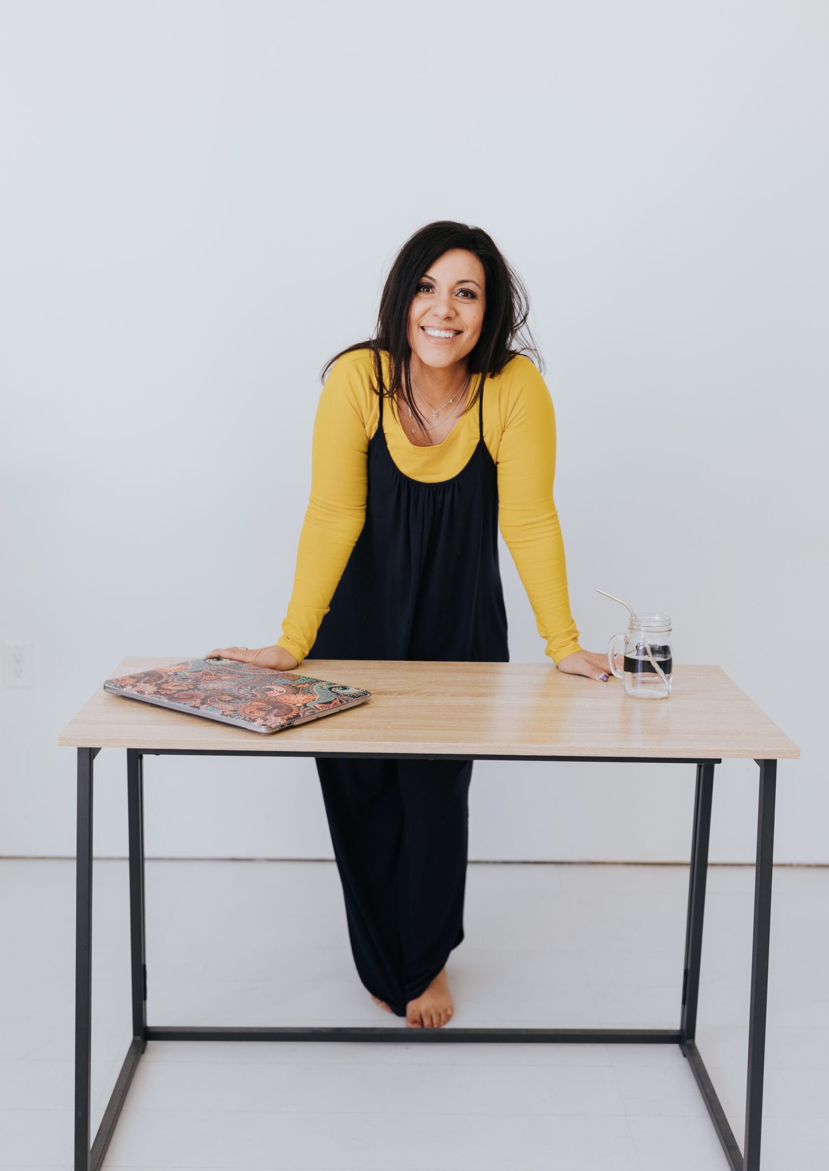 Photo of a dark haired woman standing behind a table with her laptop and a glass of water.