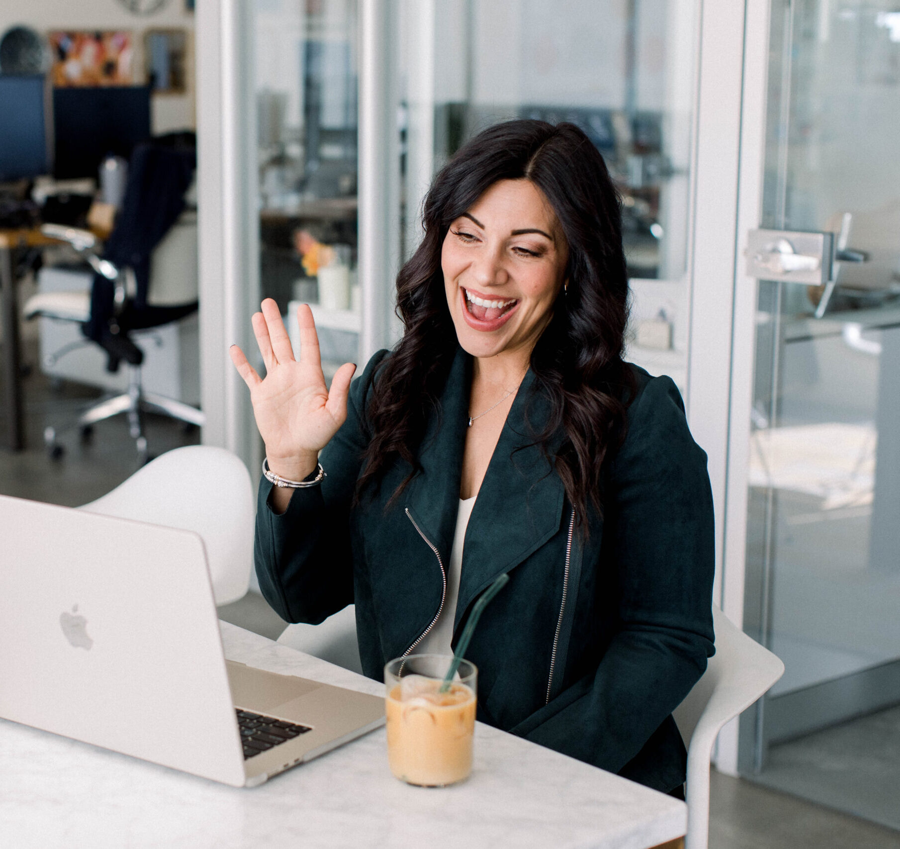 looking-at-laptop-smiling-waving-hands-in-an-office-stefanie-gass The image title is: Ep-693-Four-Ways-to-Find-Amazing-Podcast-Guests-to-Interview-Stefanie-Gass