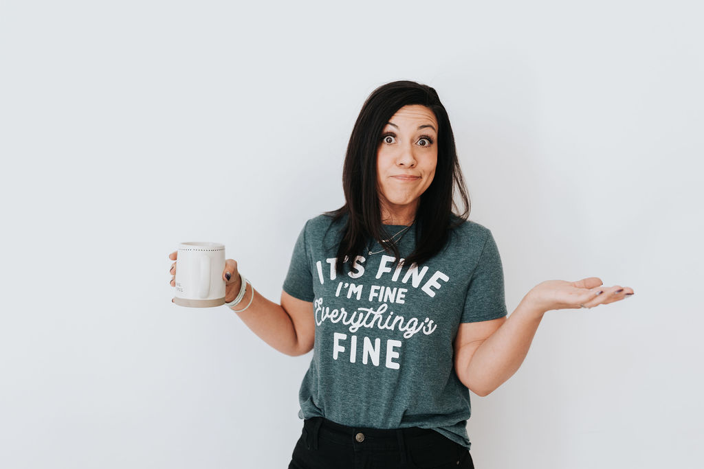 Brown haired woman standing in shock with a coffee mug, wearing a teal t-shirt.