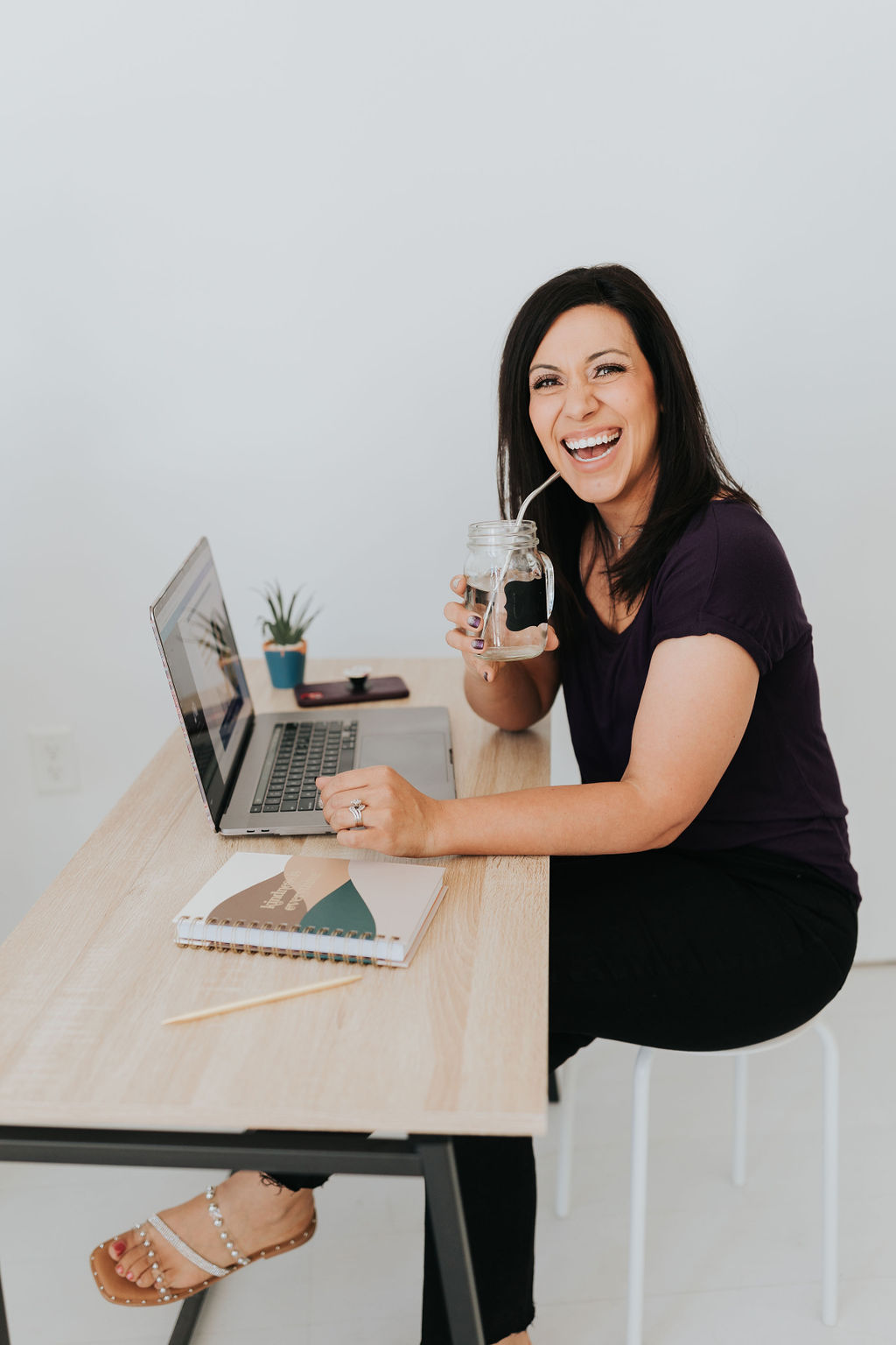 a brown haired lady smiling while working at her laptop and drinking her water