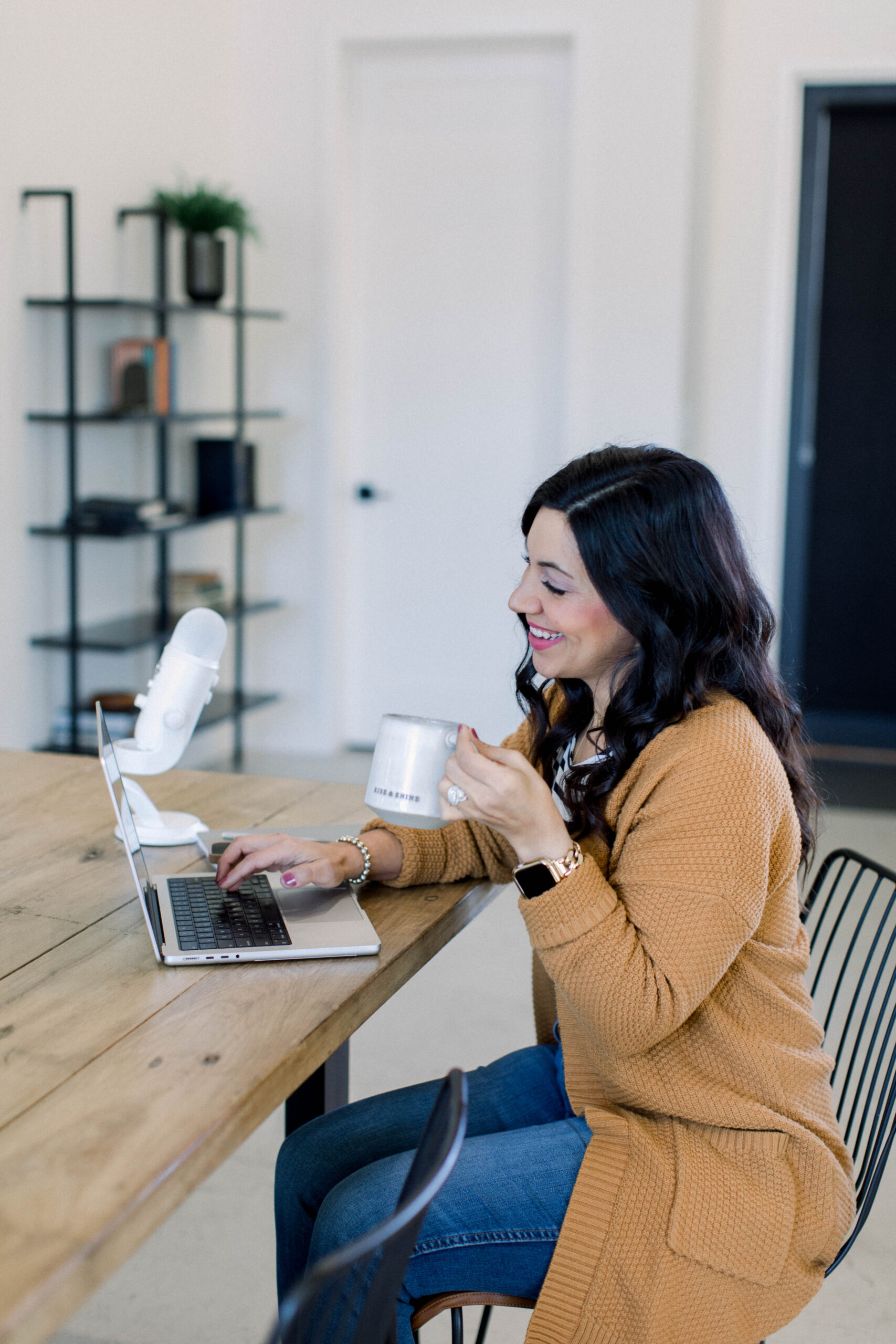 Image is a woman seated at her desk with a cup of coffee next to her podcast and laptop. 