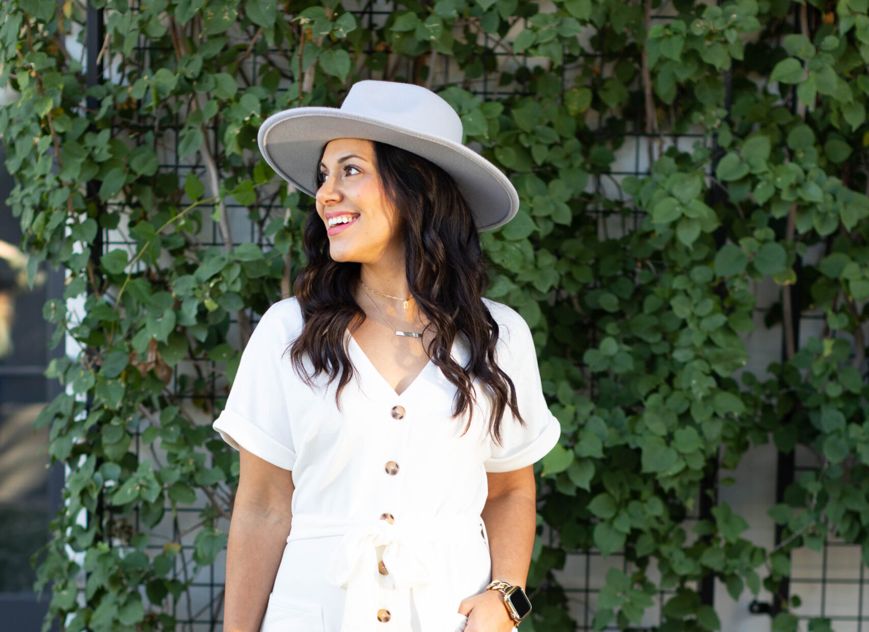 Image is a woman in white with dark hair smiling while holding a bag