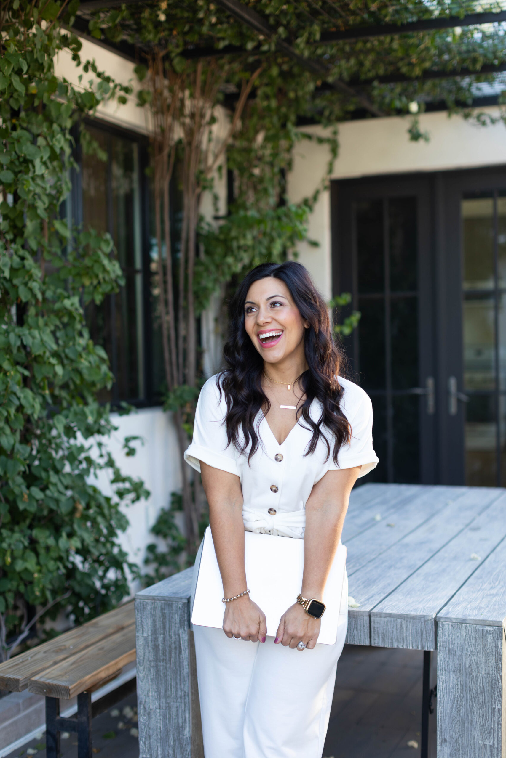 Image is a woman in white smiling while holding a laptop