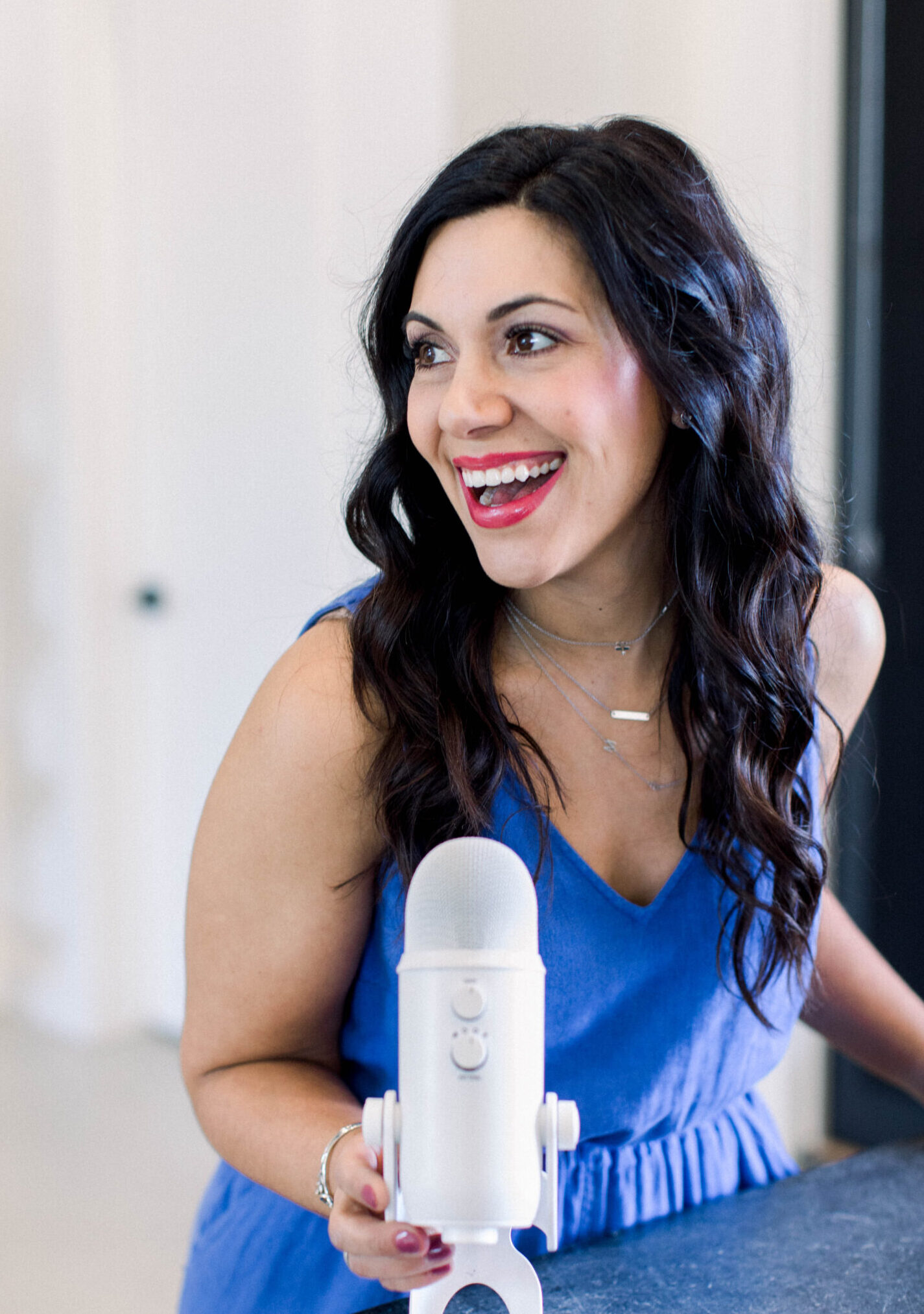 brown haired woman smiling as she leans forward toward her white podcast microphone