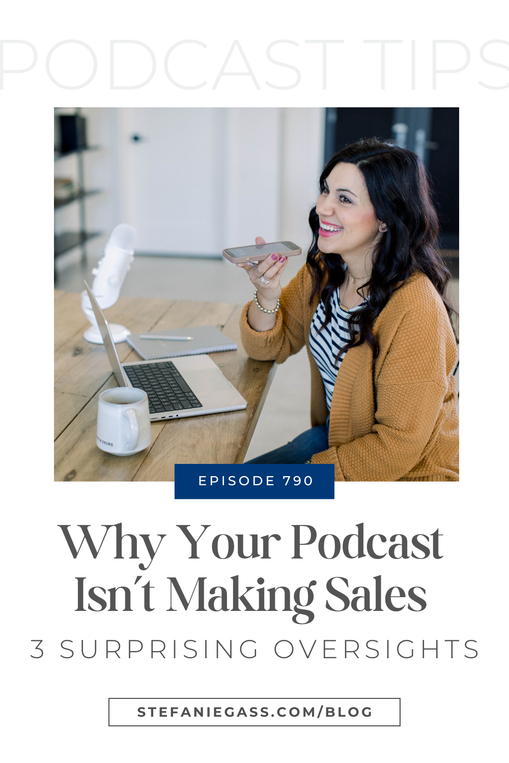 brown haired woman smiling as she talks into her cell phone. She is sitting at her desk with her laptop and white podcast microphone, Image Text reads: Why Your Podcast Isn't Making Sales 3 Surprising Oversights, Stefanie Gass Blog