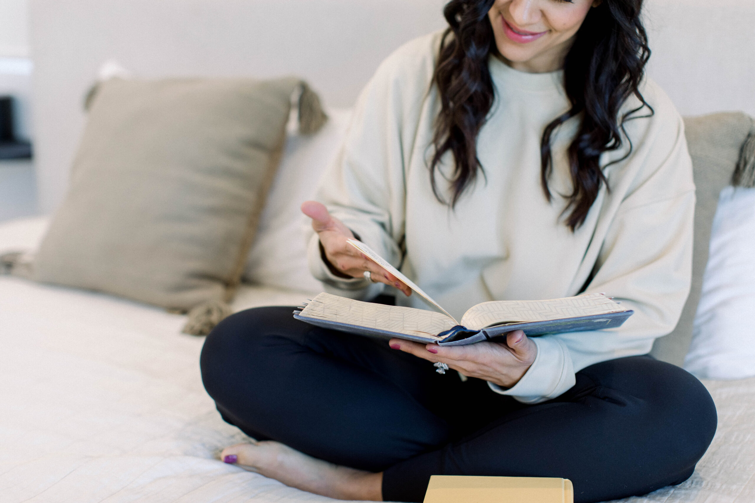 Dark-haired woman sitting in bed, crossed-legged. She's reading her bible. She's wearing a light sweater and dark leggings. The title is: Is-Your-Business-Aligned-with-God-Four-Signs-of-a-Kingdom-Business-Stefanie-Gass