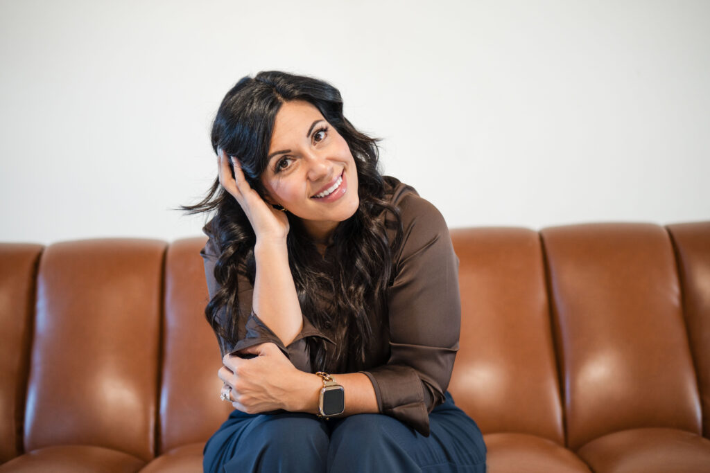 Dark-haired woman sitting on a brown leather couch. She's resting her head on her left hand. She's wearing blue jeans and a hunter-green jacket. The title is: Four-Things-I-am-Focusing-on-to-Close-The-Year-Strong-Stefanie-Gass