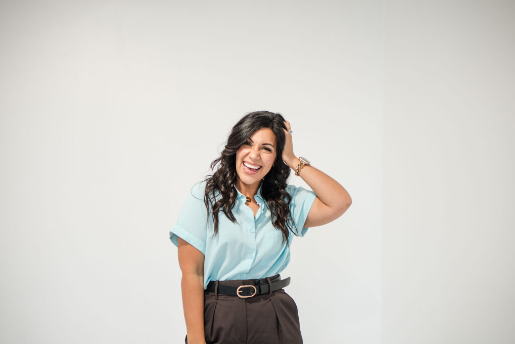 A dark-haired woman is standing in front of a blank wall. She's wearing a light blue blouse and dark pants. Her hand is against her head in a relaxed manner. The image title is: Silence-the-Noise-Overcome-Distraction-to-Hear-God's-Call-Stefanie-Gass