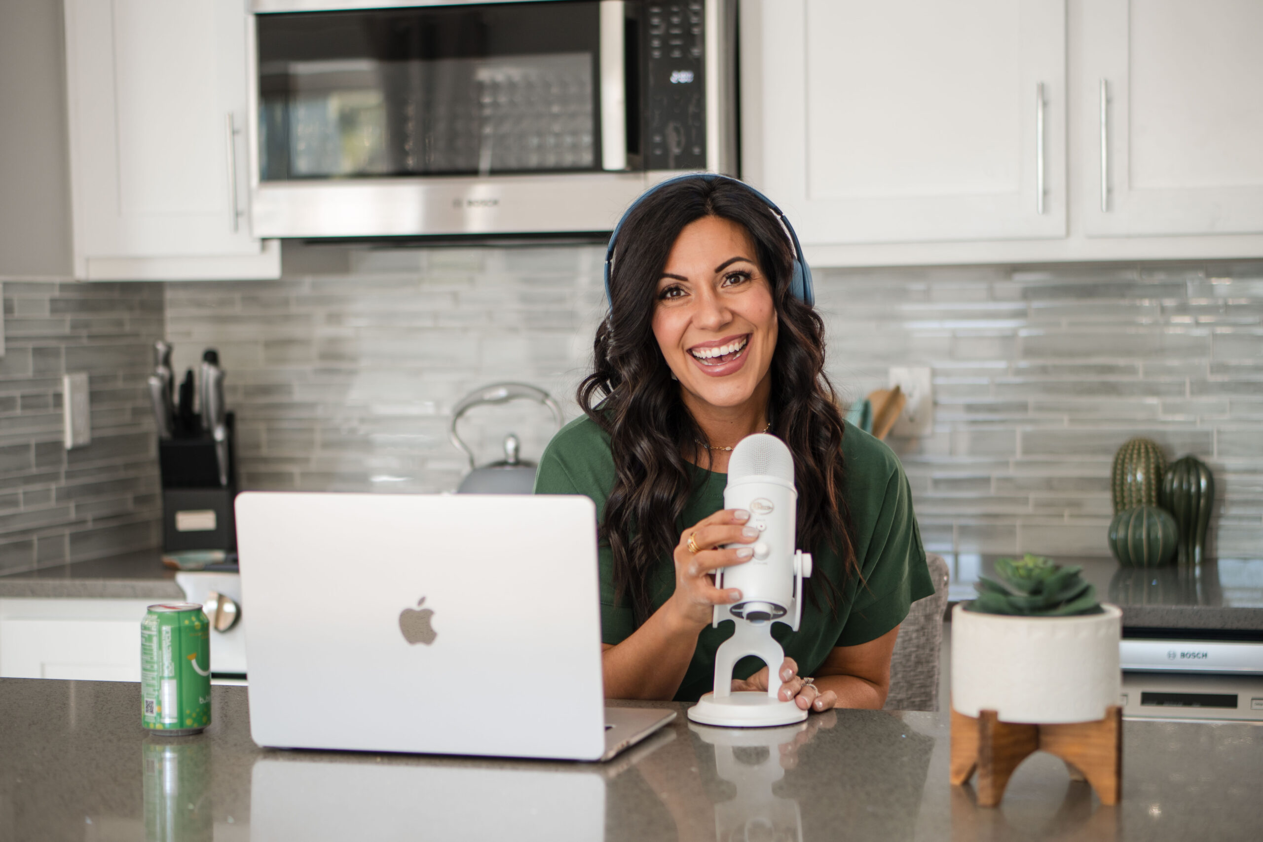 in-kitchen-front-view-holding-microphone-wearing-headphones-happy-stefanie-gass-horiztonal The post title is: How-to-Use-ChatGPT-to-Plan-Your-Weekly-Podcast-Episodes