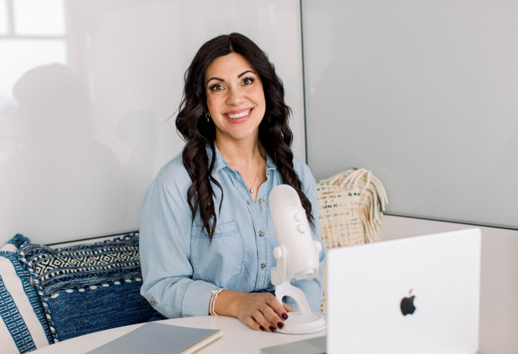 sitting-at-desk-with-microphone-smiling-stefanie-gass The image title is: Ep-828-Seasons-of-Scaling-What-to-Prioritize-at-Every-Revenue-Milestone-Stefanie-Gass