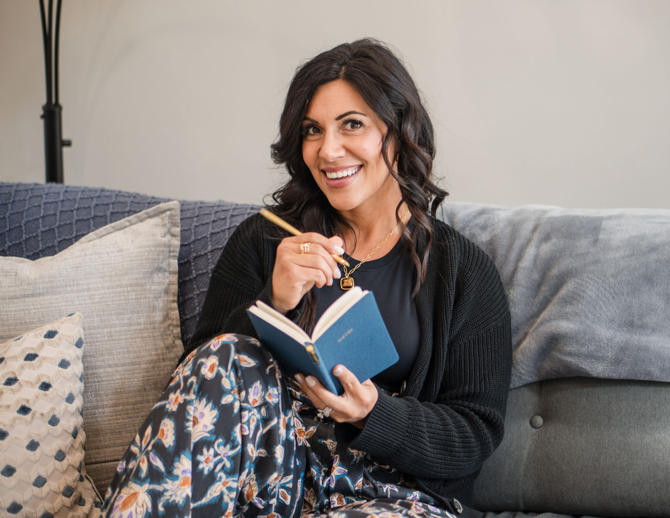 sitting-on-couch-with-knee-up-notebook-and-pen-smiling-looking-at-camera-Stefanie-Gass-horizontal The image title is: Ep-839-How-to-Pray-to-God-Over-Your-Business-Christian-CEO-Prayer-Routine-Stefanie-Gass